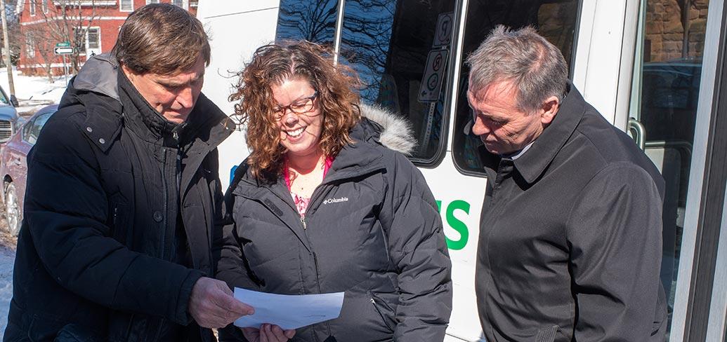 Three people in front of a transit bus looking at a document