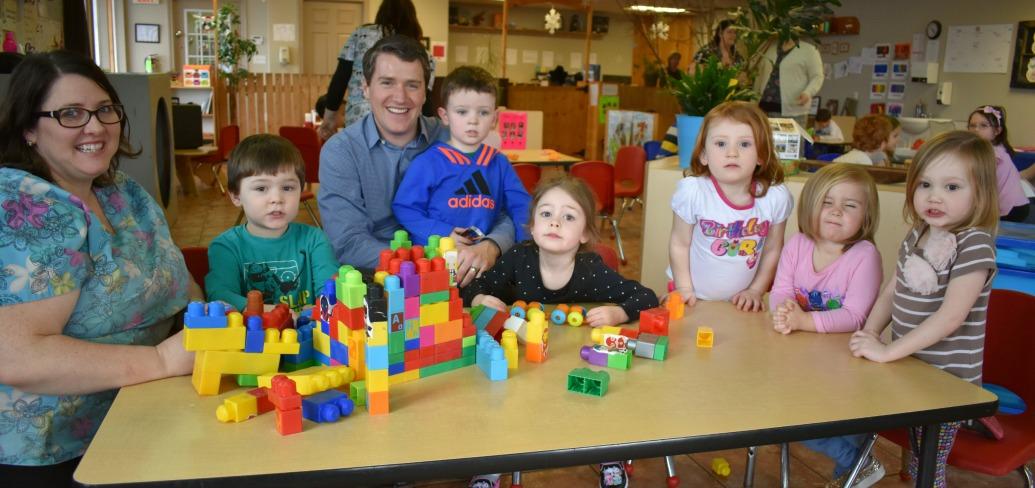 Minister Jordan Brown sits at a table with a group of day care children