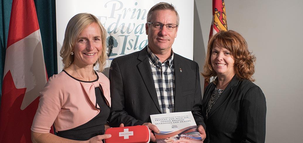 Photo shows Dr. Heather Morrisson holding a Naxolone kit, Minister Robert Henderson holding the plan, and Karen MacDonald of Justice and Public Safety.