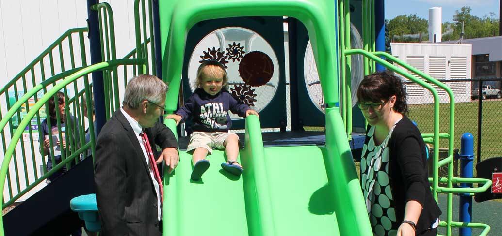 Dakota takes a slide on the new therapeutic playground while pediatric nurse manager Julie Smith and Health Minister Robert Henderson look on.
