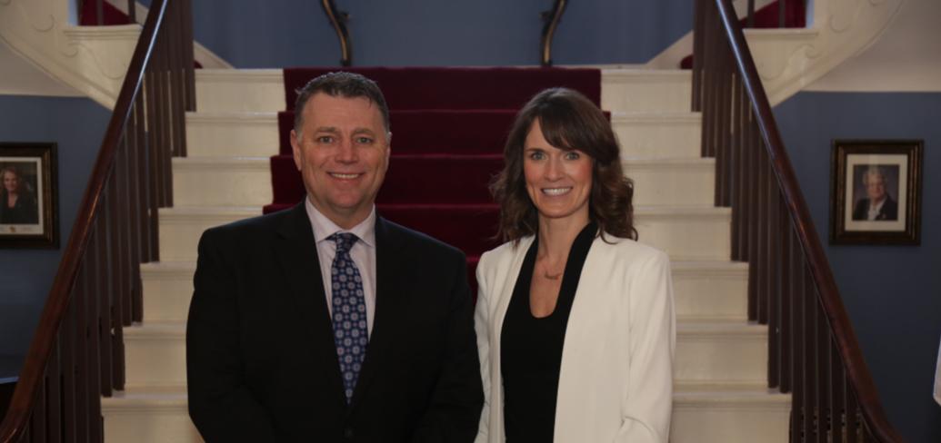 Premier King stands with Minister Jameson in front of the stairway in Government House