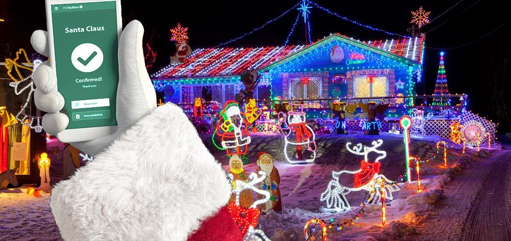 Santa's hand holding a smartphone showing his Vax Pass, with a seasonally decorated house in the background