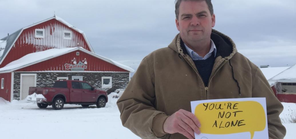 Image of Minister Bloyce Thompson in front of his barn holding a Farmers Talk sign that reads "You are not alone"