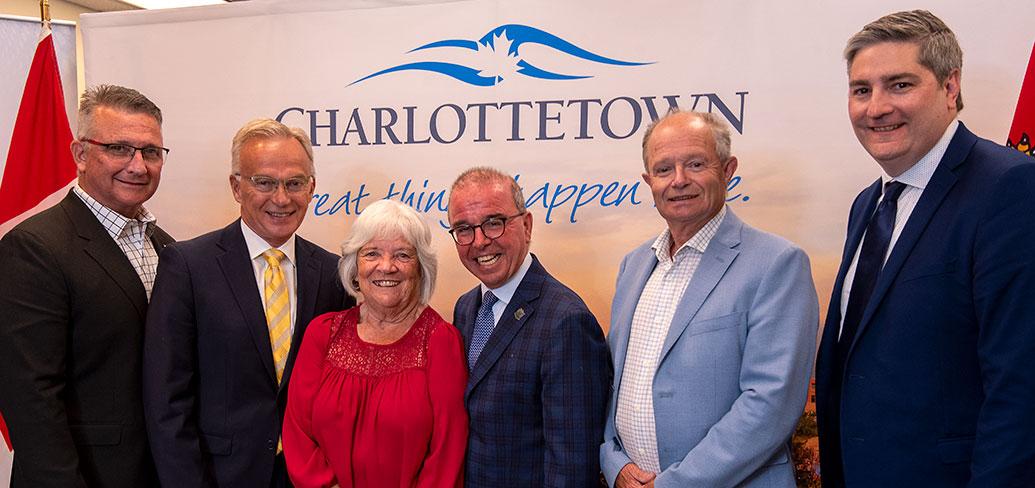 image of  a group of six people standing shoulder to shoulder in front of a City of Charlottetown sign