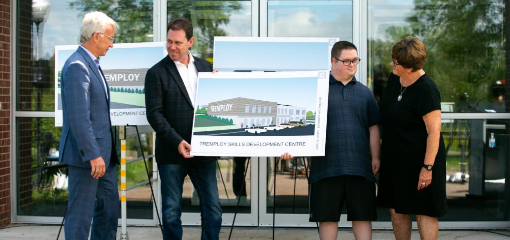 Four adults stand smiling as they look at a drawing of the new Tremploy facility to be built