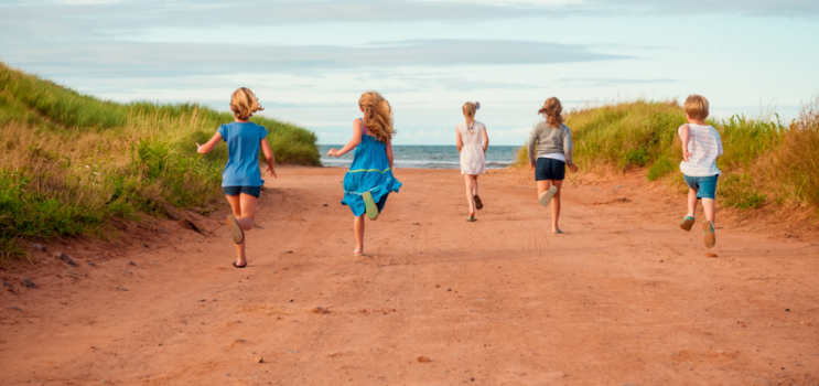 Children running down red dirt road toward a PEI beach