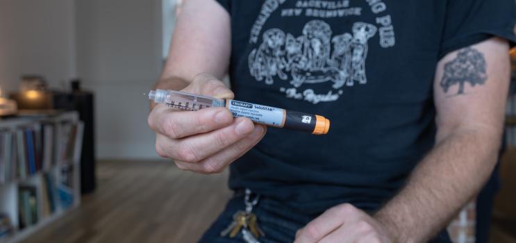 A man holds a cylinder of medicine, reading the text you can see it is an insulin injection
