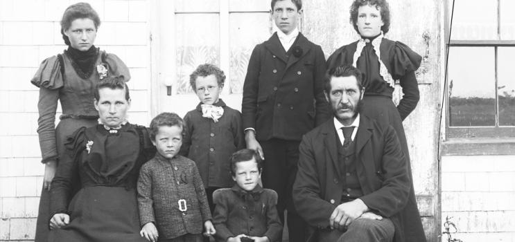 Famille constituée d’un homme, d’une femme et de six enfants prise en photo devant une maison
