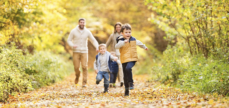 A family enjoying a walk on a trail filled with fallen leaves as two young boy runs ahead