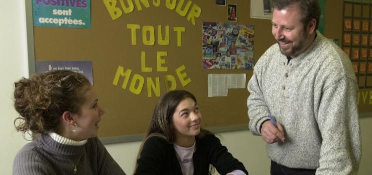Two female student speak with teacher in French classroom