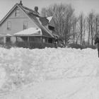 Horse and sleigh in front of house in winter, two children standing on snow bank looking at camera