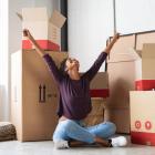 Image of a woman surrounded with empty moving boxes expressing joy as she moves into a building.