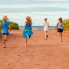 Children running down red dirt road toward a PEI beach