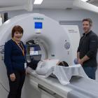 A man and a woman stand beside a large piece of medical scanning technology with a third person lying in the machinery