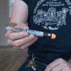 A man holds a cylinder of medicine, reading the text you can see it is an insulin injection