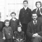 Family consisting of a man, woman, and six children posing for photograph in front of a house