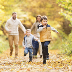Une famille profitant d'une promenade sur un sentier rempli de feuilles mortes alors que deux jeunes garçons courent devant