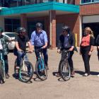 Five people sit upon bicycles in front of the Charlottetown Police Station; three people stand beside them
