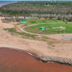 aerial photo of a beach area with rocks in front and a lighthouse in the background
