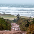 image of a red dirt road leading down a hill toward the water while waves are crashing onshore