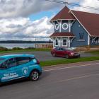 image of an electric vehicle on a street with a building and a bay in the background