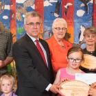 Photo shows Minister Brown surrounded by adults and children holding wooden plaques