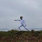 image of a person  outside on a small hill by the water practicing the sport of fencing