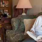 Photos shows Gladys Dirani sitting in her living room with a book on her lap.