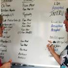 Photo shows two women talking in front of a whiteboard