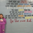  image d'un enseignant et d'élèves du primaire debout près d'un mur avec des écrits inspirants dessus.