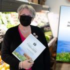 Finance Minister Darlene Compton is standing in a local grocery market holding a copy of the budget