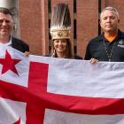 image of three people standing shoulder to shoulder holding a flag in front of them