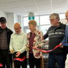 image of six people in a room standing shoulder to shoulder and one person is cutting a ribbon held by all of them