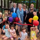 image of a group of younger and older people  cutting an ribbon in front of new playground equipment