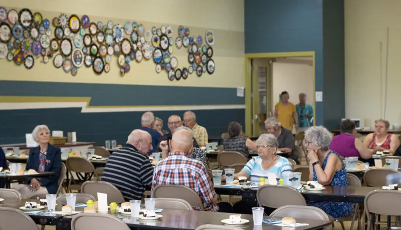 Seniors seated at tables during a community meal.