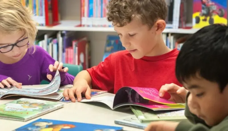 trois jeunes enfants assis à une table en train de lire des livres