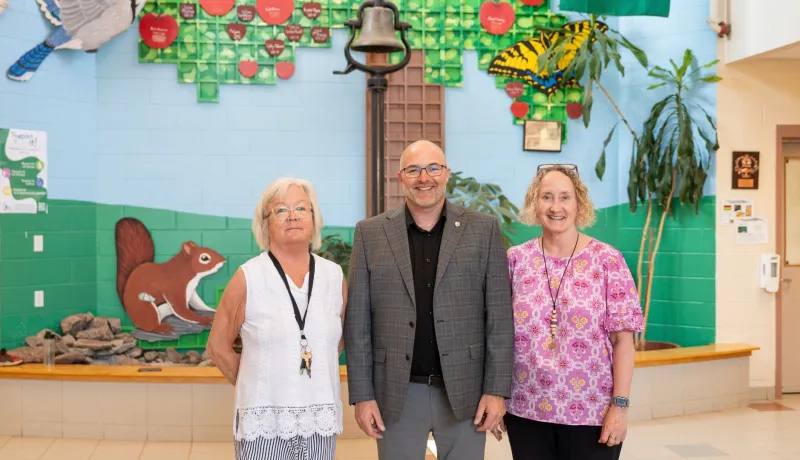 Two women and a man stand in front of a colorful mural.