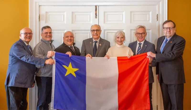 Sept personnes tiennent un grand drapeau acadien.