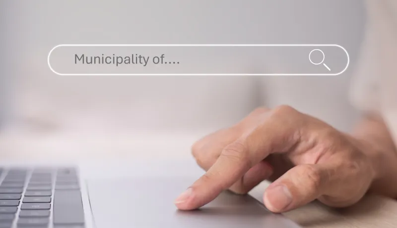 A person&#039;s hand resting on a laptop keyboard, with the screen displaying a search bar reading &quot;municipality of.&quot; 