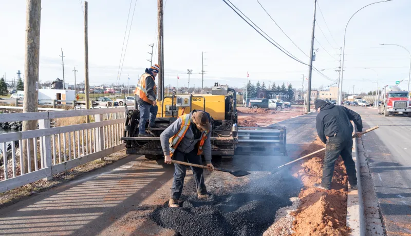 Three construction workers placing asphalt on an active transportation pathway in Prince Edward Island.