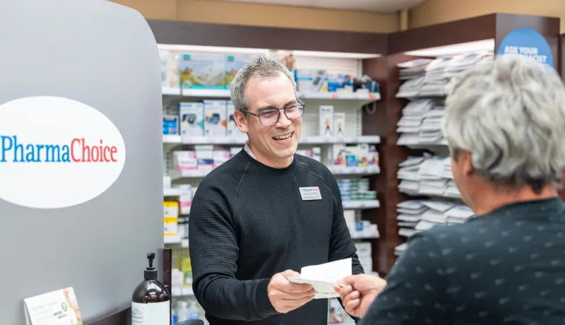 A pharmacist hands a prescription to a woman.