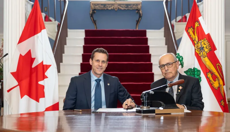 The premier and the lieutenant governor seated between two flags.