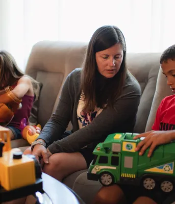 adult sitting on a couch playing with two children with toys