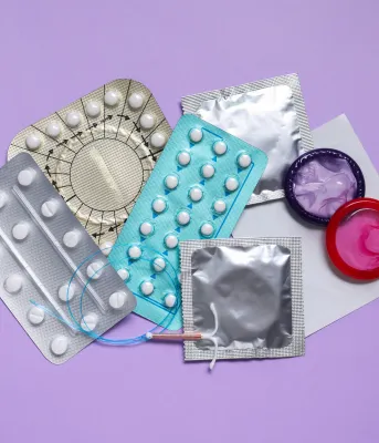 Different contraceptives laid out together with a lilac backdrop.