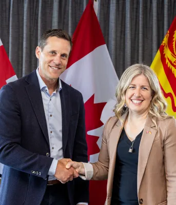 The Premiers shake hands in front of the PEI, New Brunswick and Canadian flags.