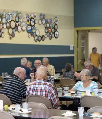 Seniors seated at tables during a community meal.