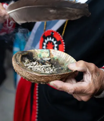 One hand holds a smudge bowl and the other hand holds a feather.