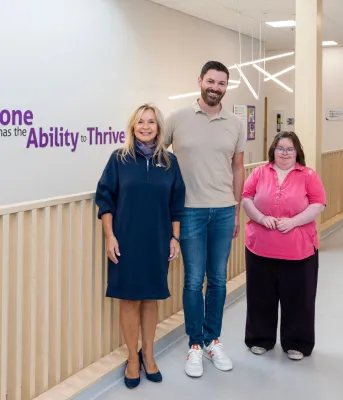 Three people stand in front of a wall with a motivational quote.