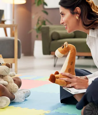 A woman and girl smiling and talking to each other while sitting on the floor holding plush animal toys and a clipboard.