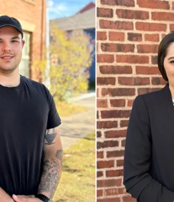 A photo of a man and a woman with brick a building behind them.